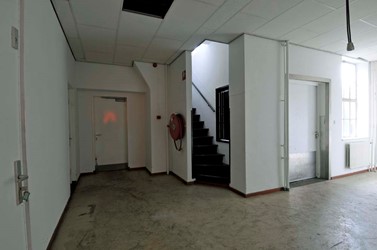 <p>De dienstvertrekken waren geconcentreerd in het centrale gedeelte tussen de twee vleugels. Overzicht van het knooppunt van de dienstgang, met centraal links de diensttrap naar de officiersmess en rechts de dienstingang aan het binnenterrein. De gang rechts leidt naar de dienstvertrekken bij de onderofficiersmess. Rechtdoor geeft een deur toegang tot het buffet van de manschappenkantine. </p>
